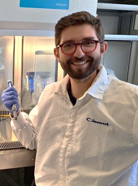 Bearded man with glasses wearing a lab coat and smiling at the camera