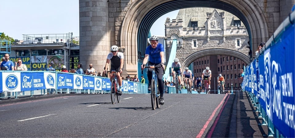 Man cycles across tower bridge wearing a DEBRA cycling jersey