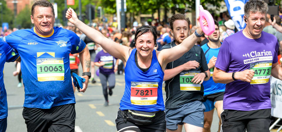 Woman crosses the Leeds 10k finish line with her hands in the air. Surrounded by other smiling runners.