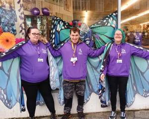 3 members of team Bathgate standing outside the front of the shop wearing purple hoodies and blue butterfly wings.