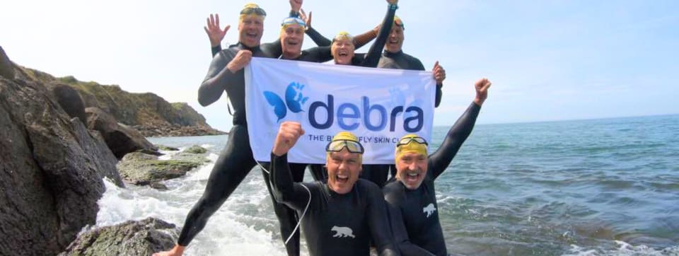 Graeme Souness, Andy Grist and Channel Swim team celebrate on the French coast wearing wetsuits and holding a DEBRA banner