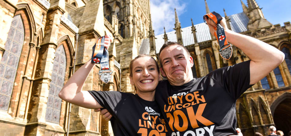Two runners hold up their Lincoln 10k medals with Lincoln cathedral in the background.