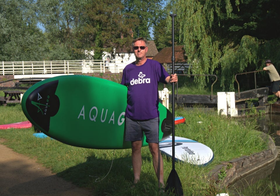 100km challenge participant holding paddleboard in DEBRA t shirt