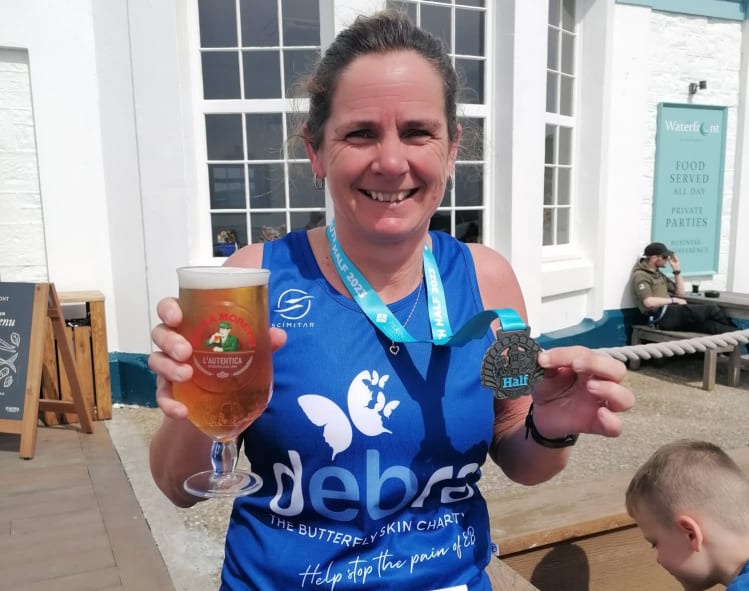 Runner smiles holding a medal and her pint at the finish line.
