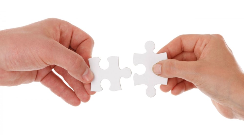 two hands putting together two puzzle pieces