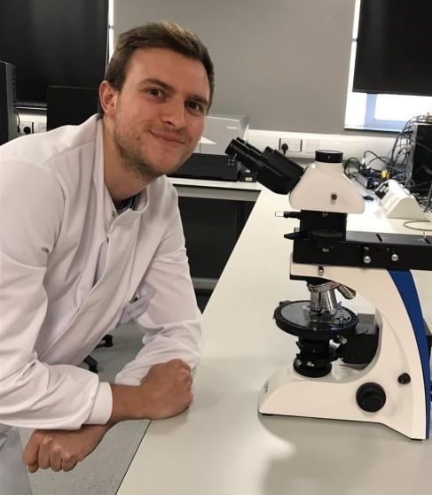 Dr Tom Robinson wearing a lab coat next to a microscope