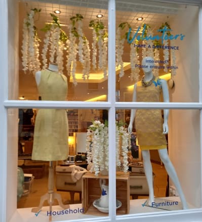 DEBRA Bridge of Allan window display with two female mannequins wearing short yellow dresses with a white flower backdrop