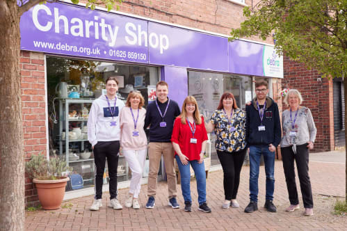 7 members of the DEBRA Poynton Team standing outside the charity shop smiling