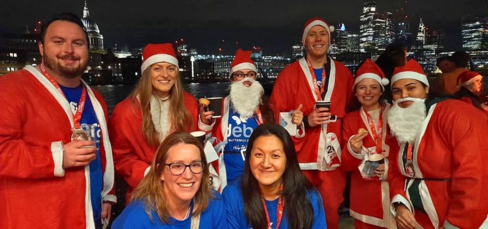 Team dressed in Santa suits hold up medals after completing Santa in the City
