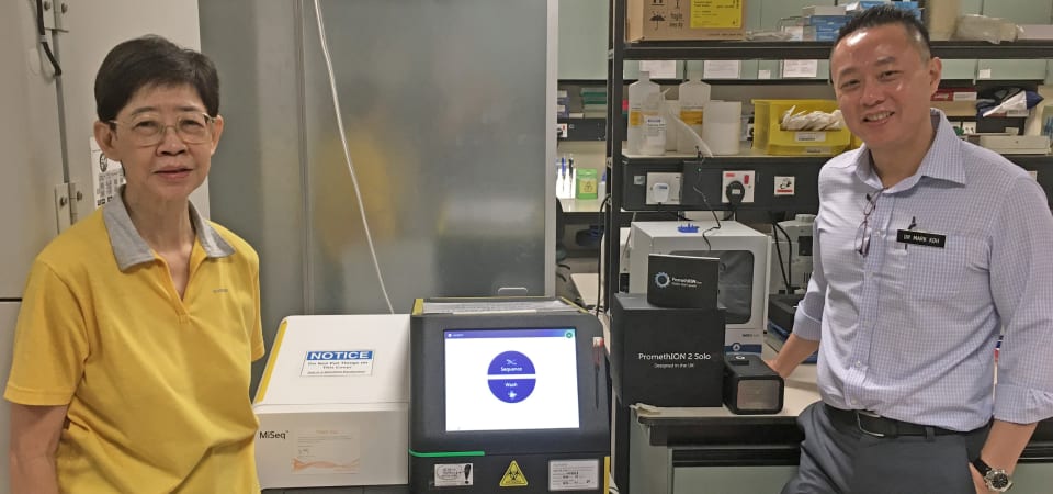 Dr Koh with the long-read sequencer on his right and Dr Tan (in yellow) with the machine for short-read sequencing on her left: Two people in a laboratory with molecular genetics equipment.