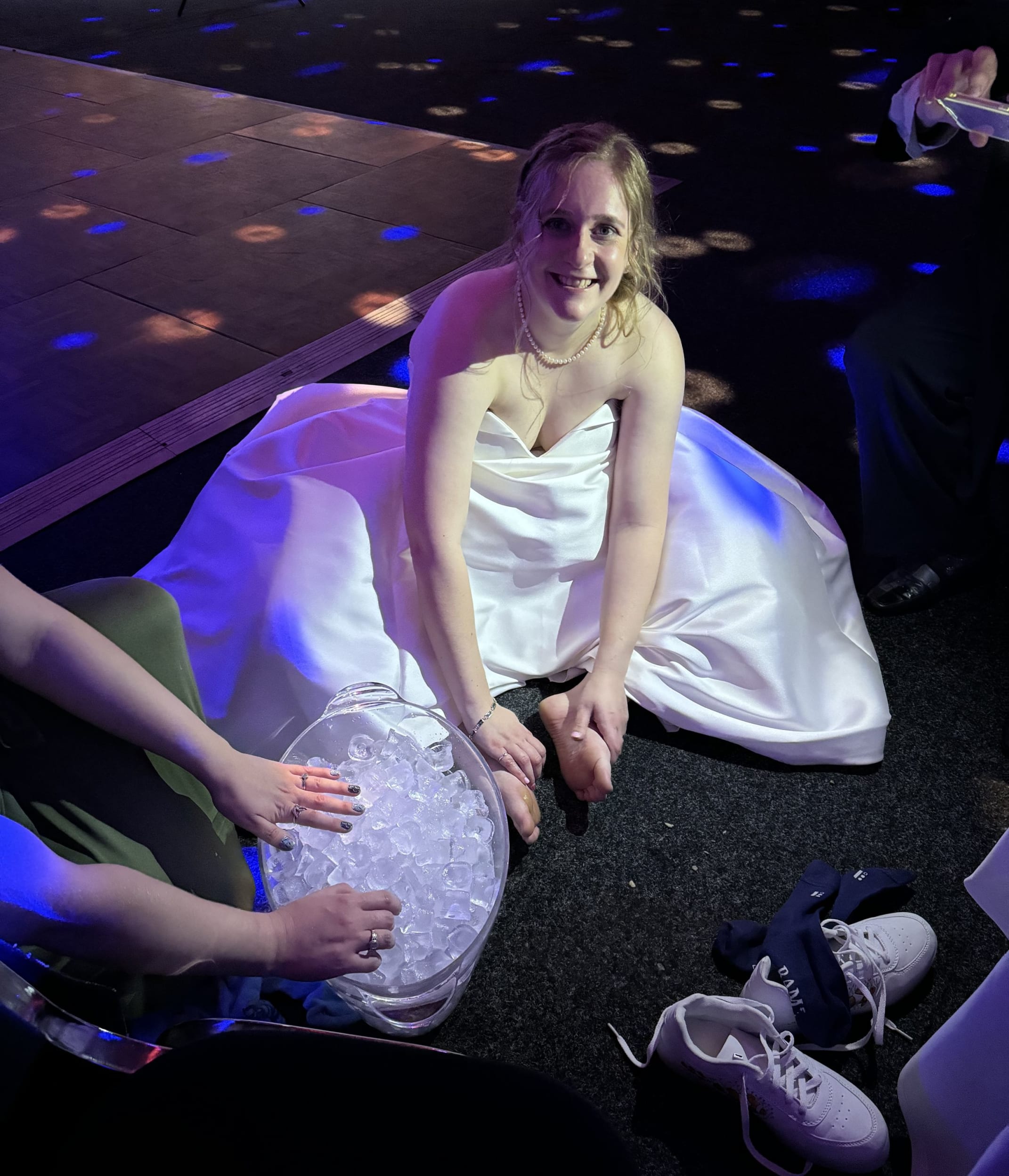 Heather sitting on the floor in her wedding dress with an ice bucket for her feet